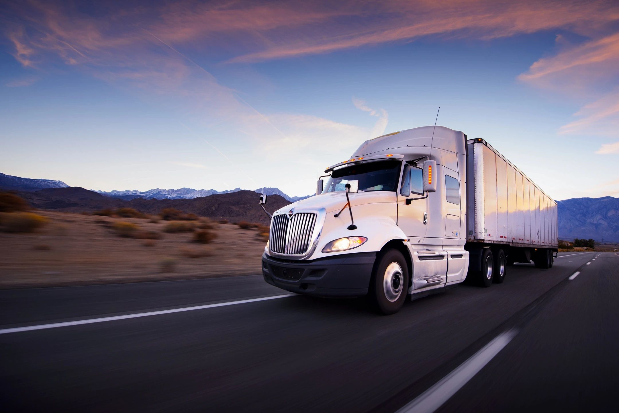 Premier Carriers semi-truck driving on a highway through a desert landscape at golden hour